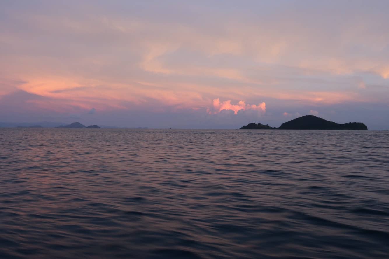 Ocean with a pink sky and a tiny island in the distance