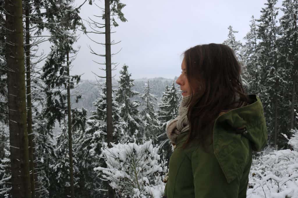 Side portrait of a girl with a kaki coat in a snowy landscape with pines 