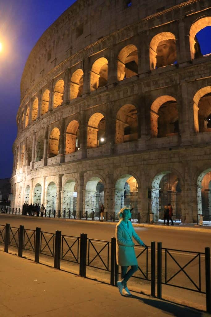 Tiny blond girl looking up at the huge Colosseum at night