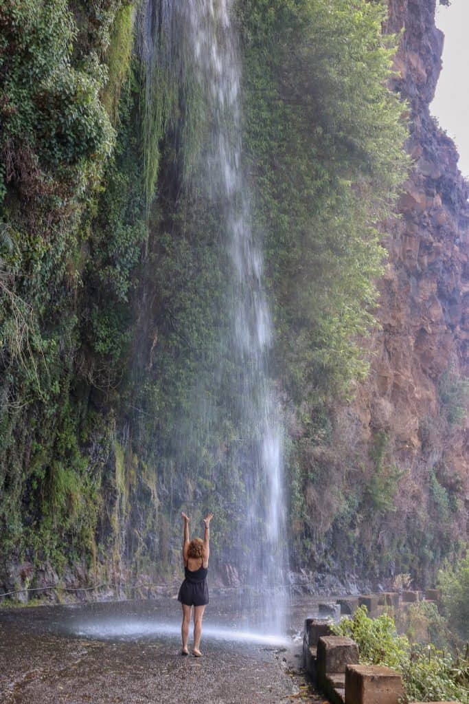 Girl with her hands up standing in the middle of the street under a waterfall