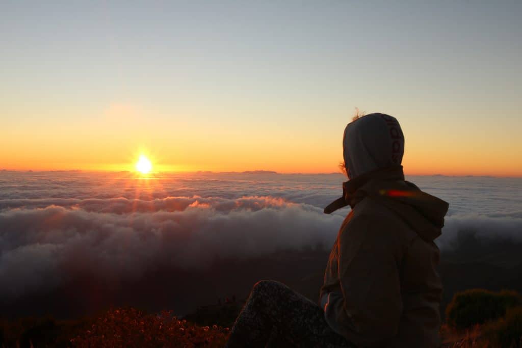 Girl with her hoodie on looking at the sunrise and the clouds on a mountain