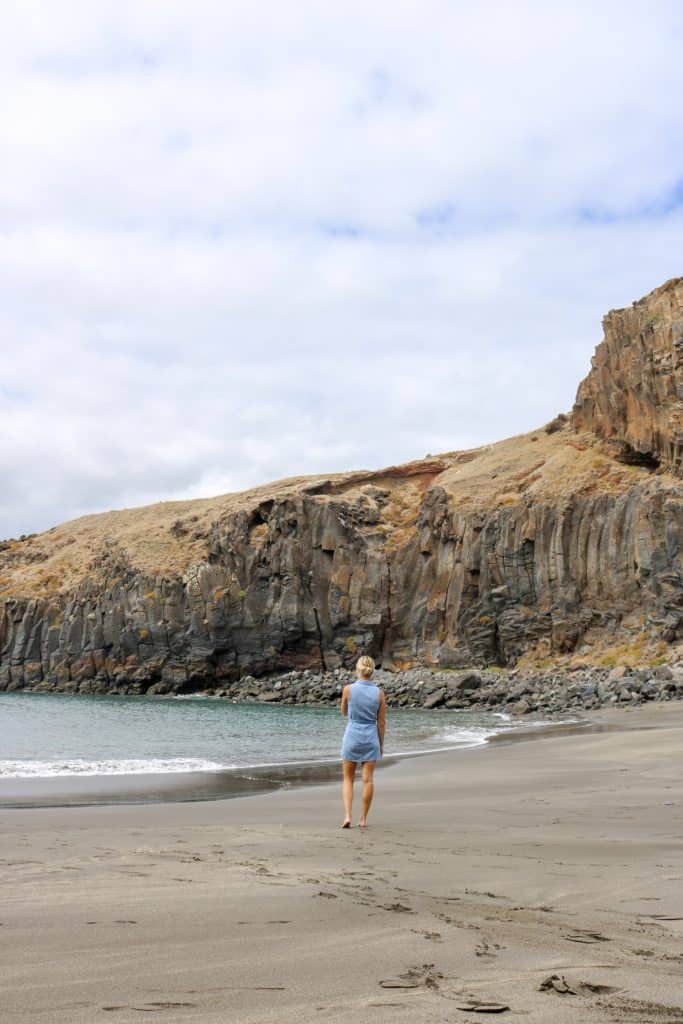 Blonde girl in a jeans dress walking on a beach with gray sand