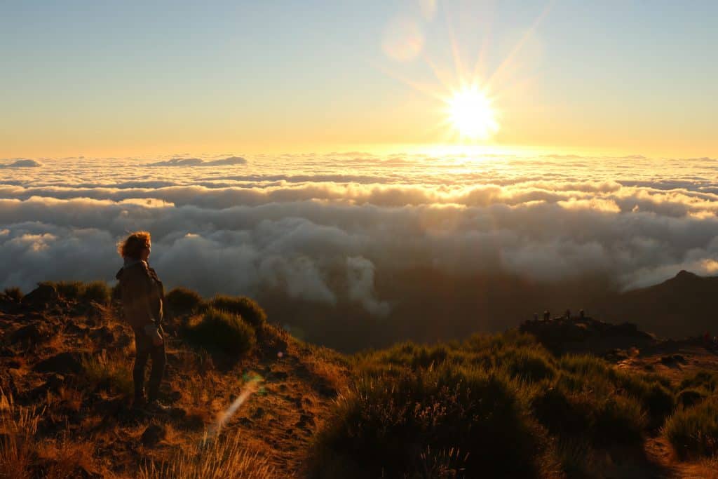 Girl on the top of a mountain watching the sunrise and overlooking the clouds