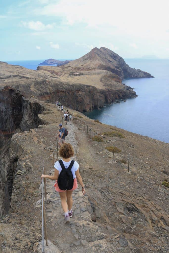 Girl in pink shorts and a black backpack descending a paved path on a hike in Madeira