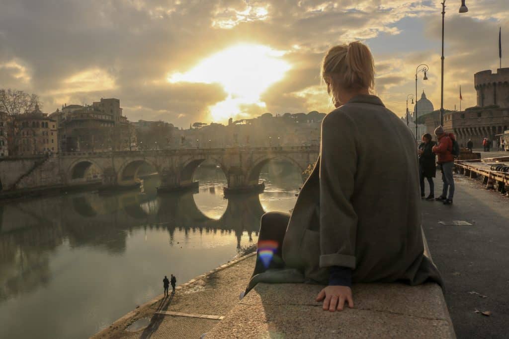 Girl sitting on a wall watching the sunset over the angel bridge