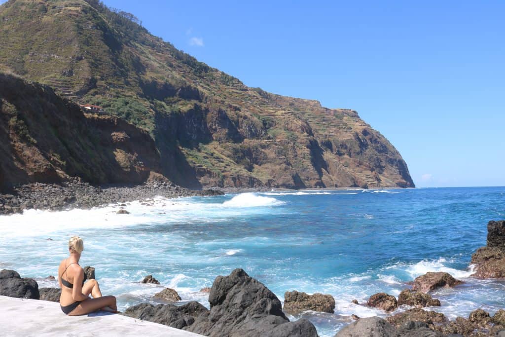 Girl sitting at the edge of the pool overlooking the ocean and a mountain