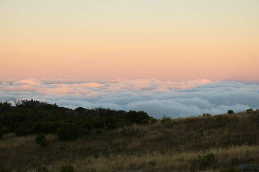 Green mountain view with clouds in colors of pink and yellow because of the sunset