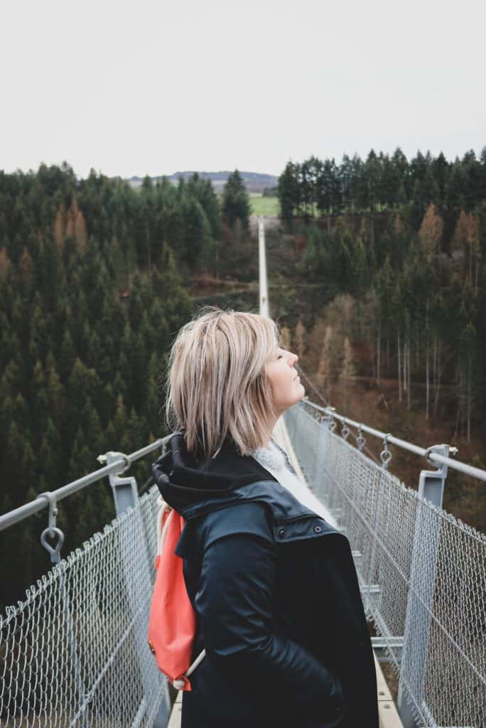 Side portrait of a girl looking up, but with her eyes closed standing on a long suspension bridge