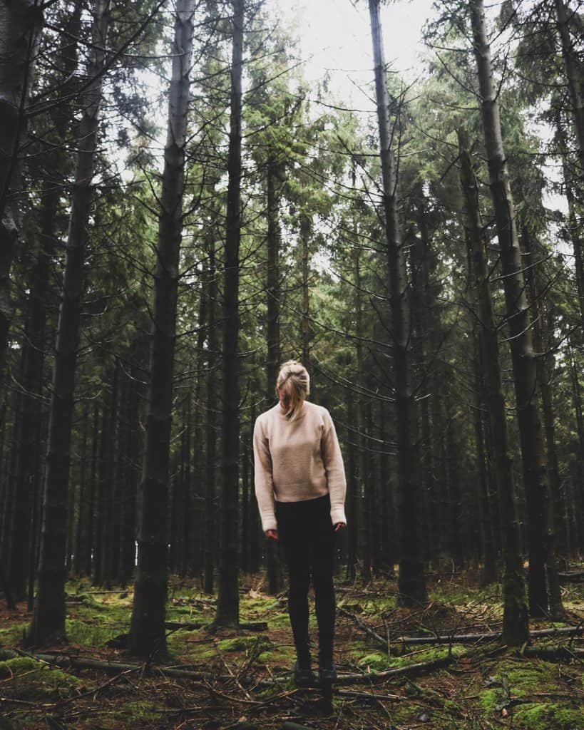 Blonde girl standing in the middle of a forest and high pine trees