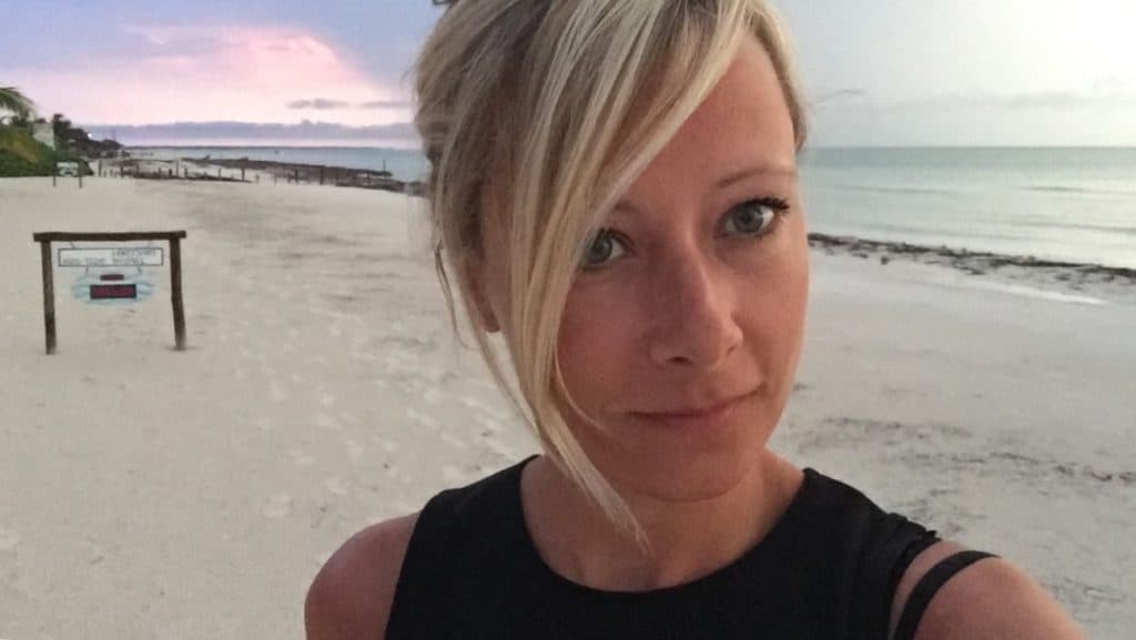 Selfie of a blonde girl on the beach with a pink sunset behind her