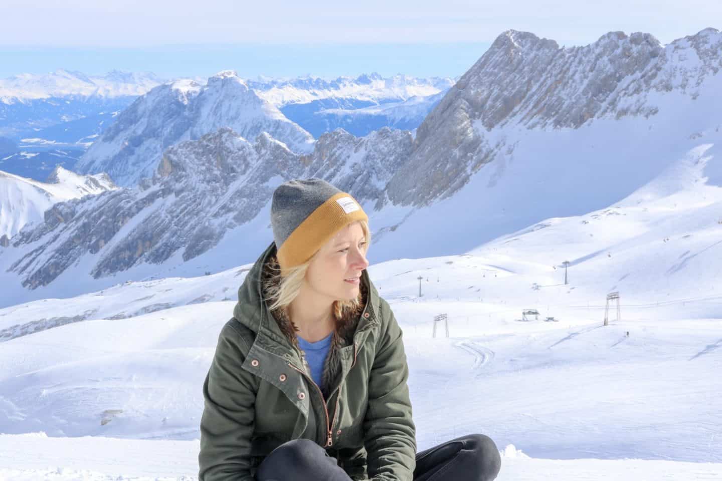 Blonde girl with hat on in front of a snowy mountain