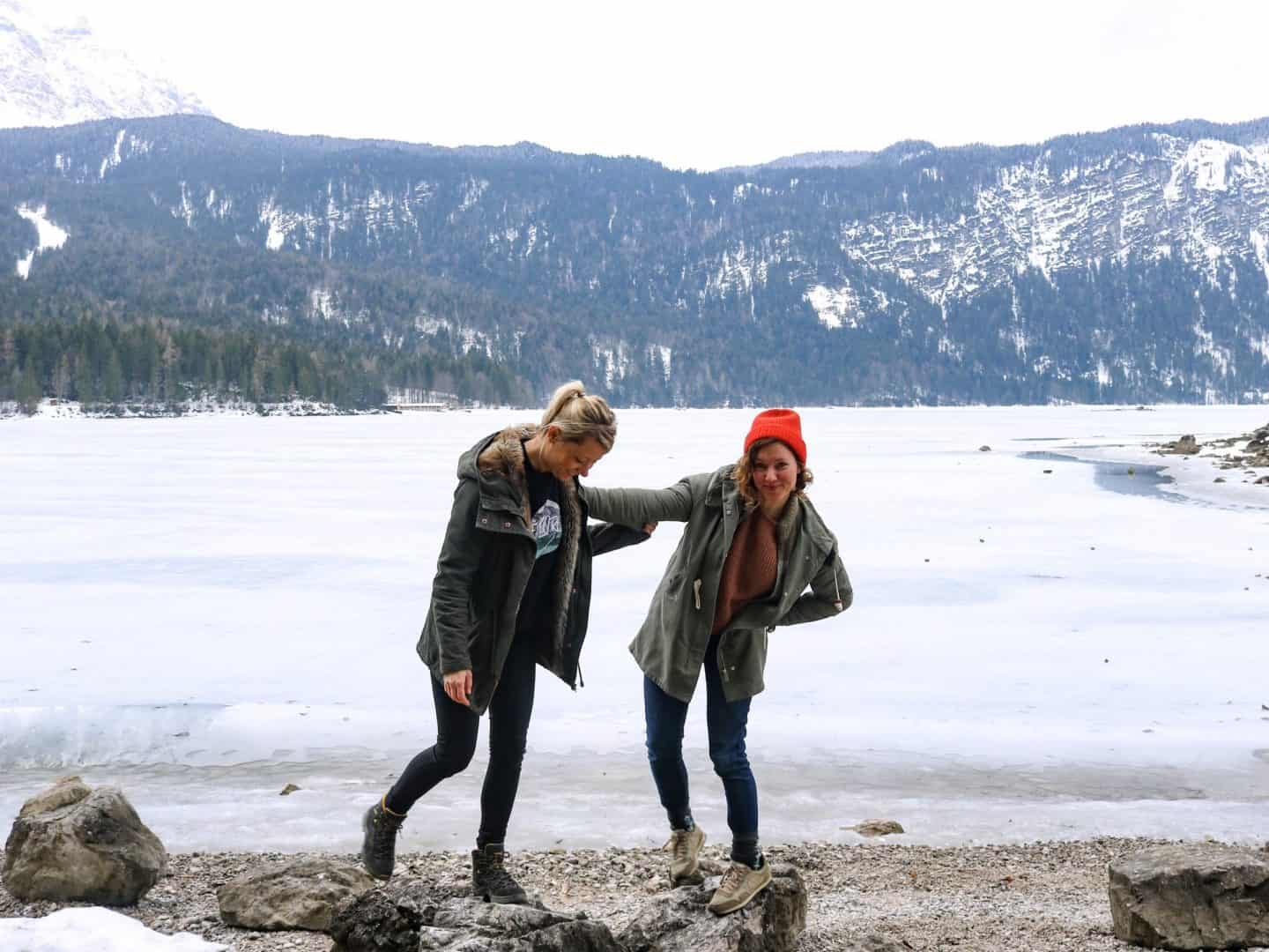 Two girls pushing eachother in front of a frozen lake