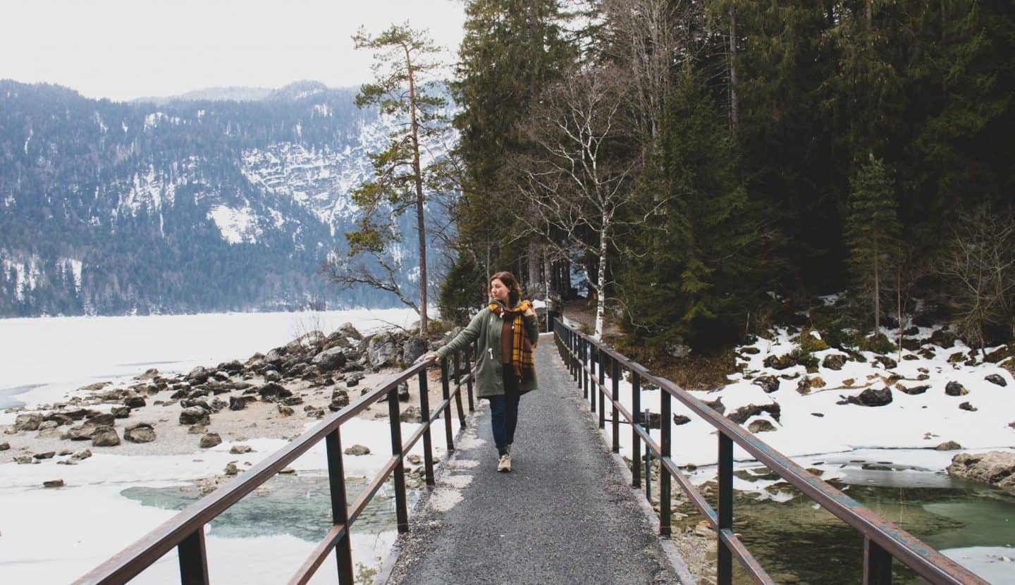 Girl on a bridge over a frozen lake with trees behind her