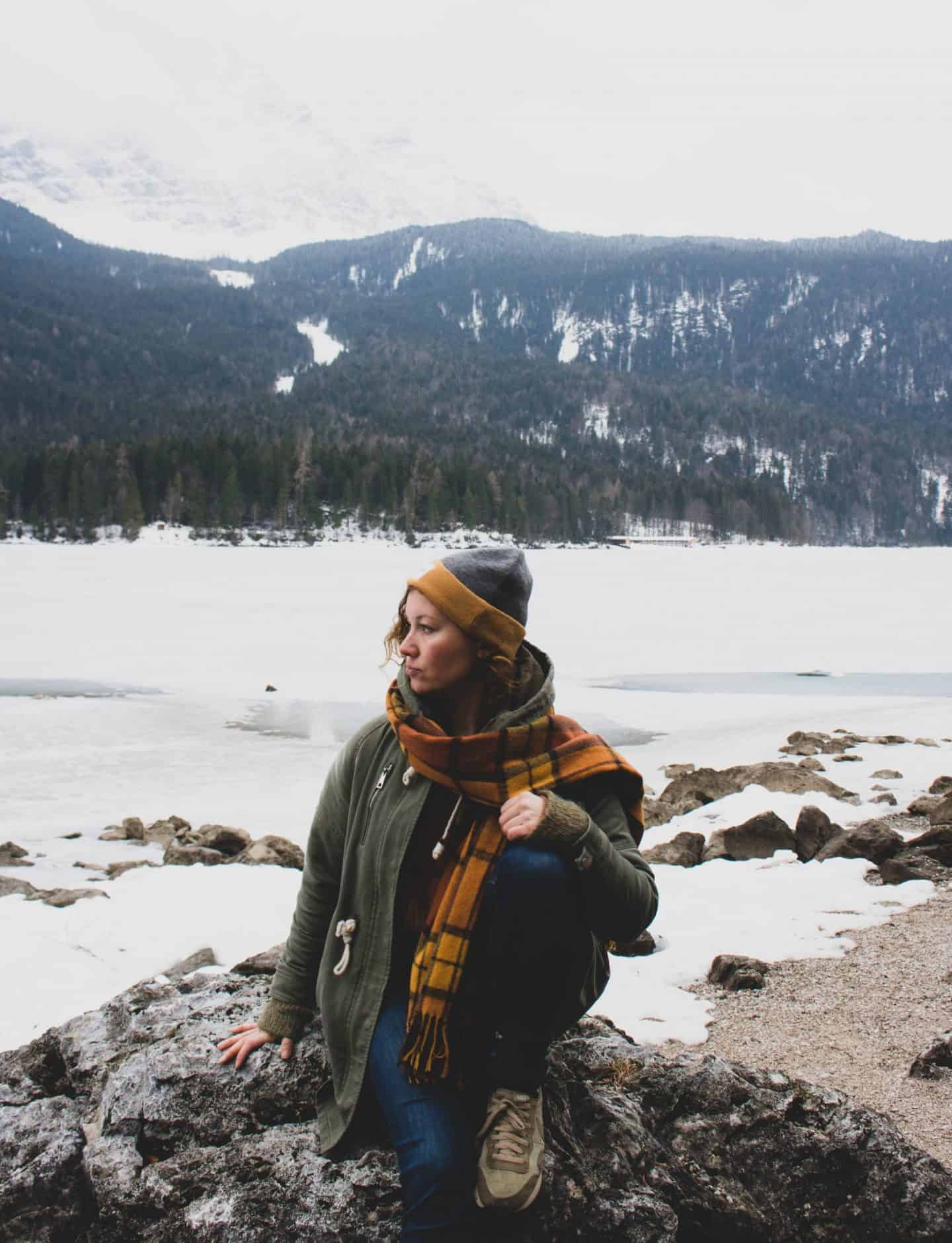 Girl with hat on and green jacket in front of a frozen lake