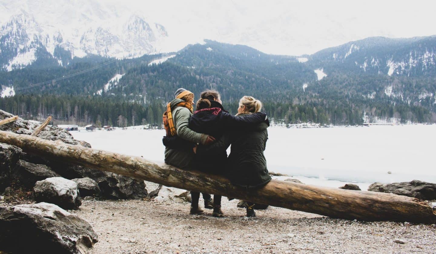 3 girls on a tree branch in front of a frozen lake