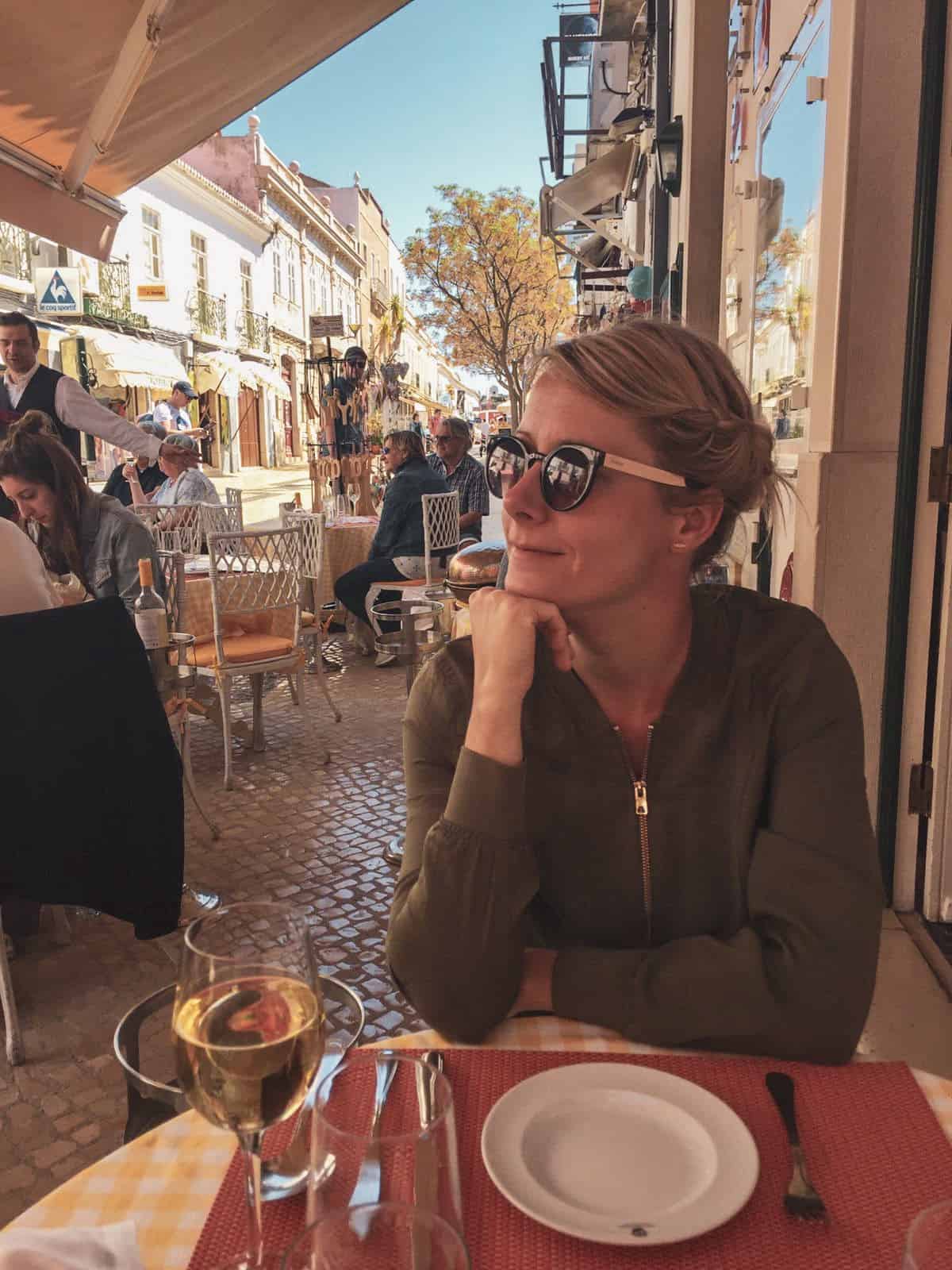 Girl on a terrace in Algarve waiting for food with a glass of wine